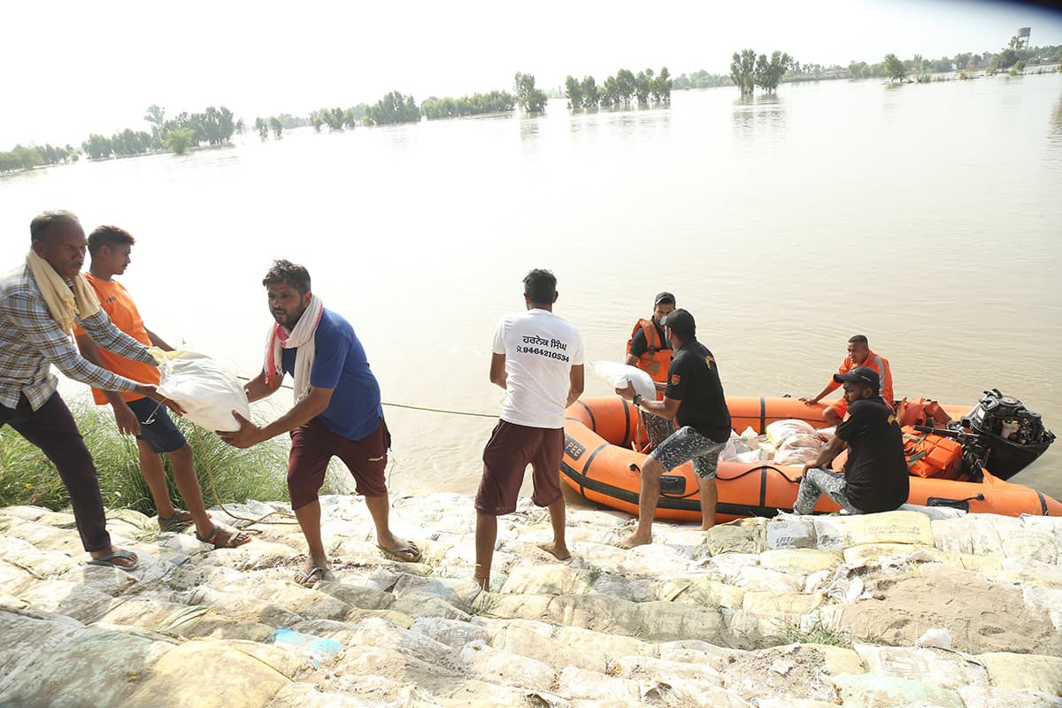 Volunteers forming a chain to pass relief sacks up a sandbagged embankment from a rescue boat