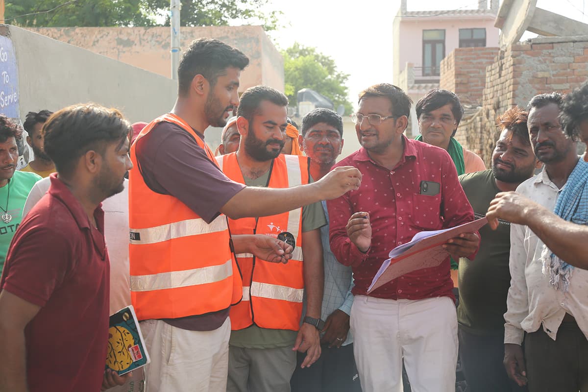 Joti Foundation responders in hi-vis vests talking with residents around a clipboard during a needs assessment