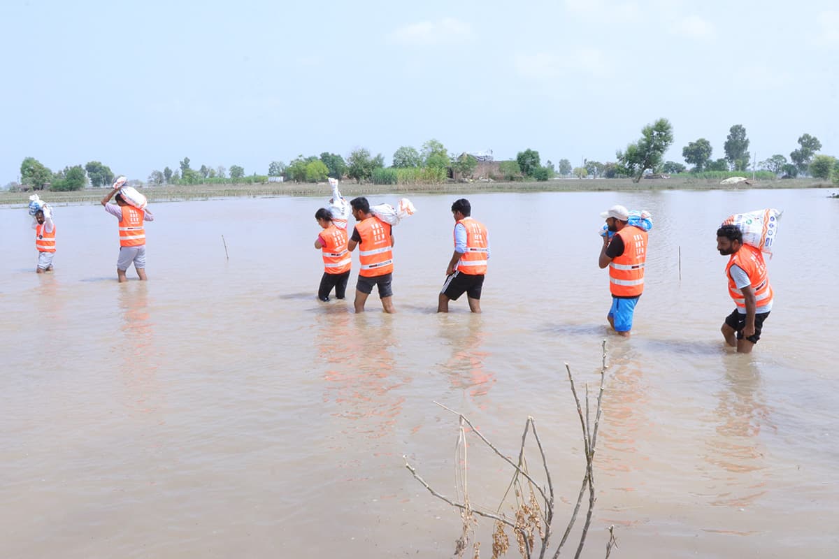 A line of relief workers wading through floodwater carrying supply sacks