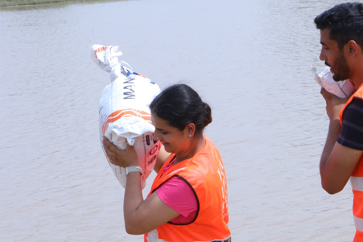 A Joti Foundation volunteer smiles while carrying a relief supply sack beside floodwaters