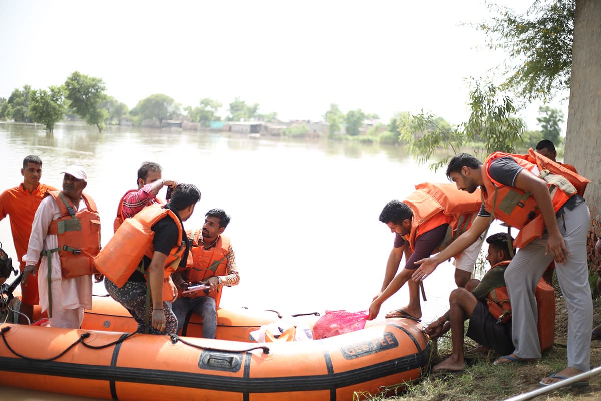 Responders in life jackets loading supplies into an inflatable rescue boat at a flooded riverbank